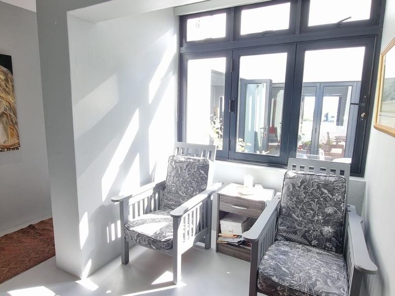 A bright, sunlit seating area featuring modern dark-framed windows and neutral tiled flooring, creating a comfortable and inviting space.