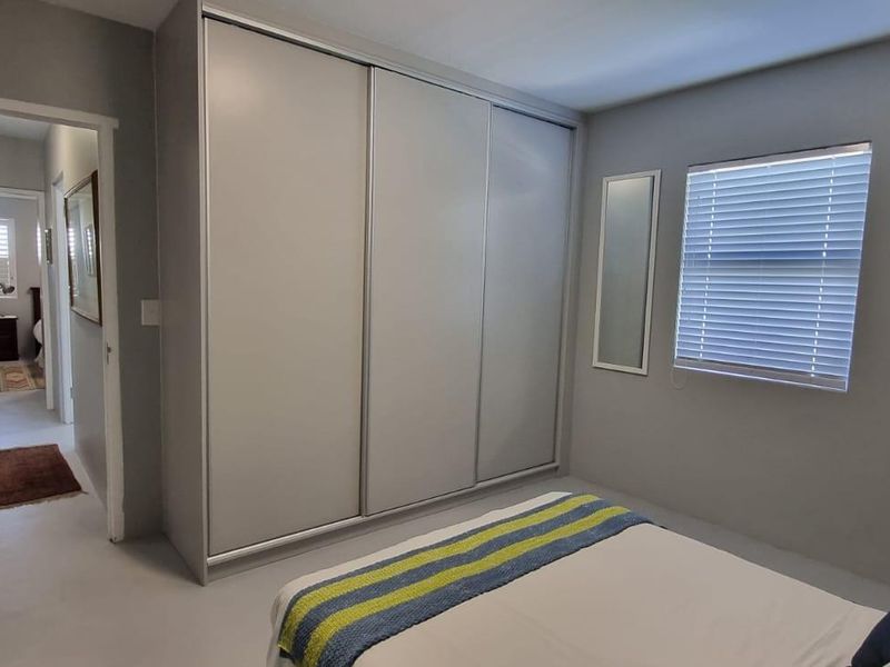 A well-maintained bedroom featuring a large built-in sliding door wardrobe and venetian blinds, with a view into the adjacent hallway.