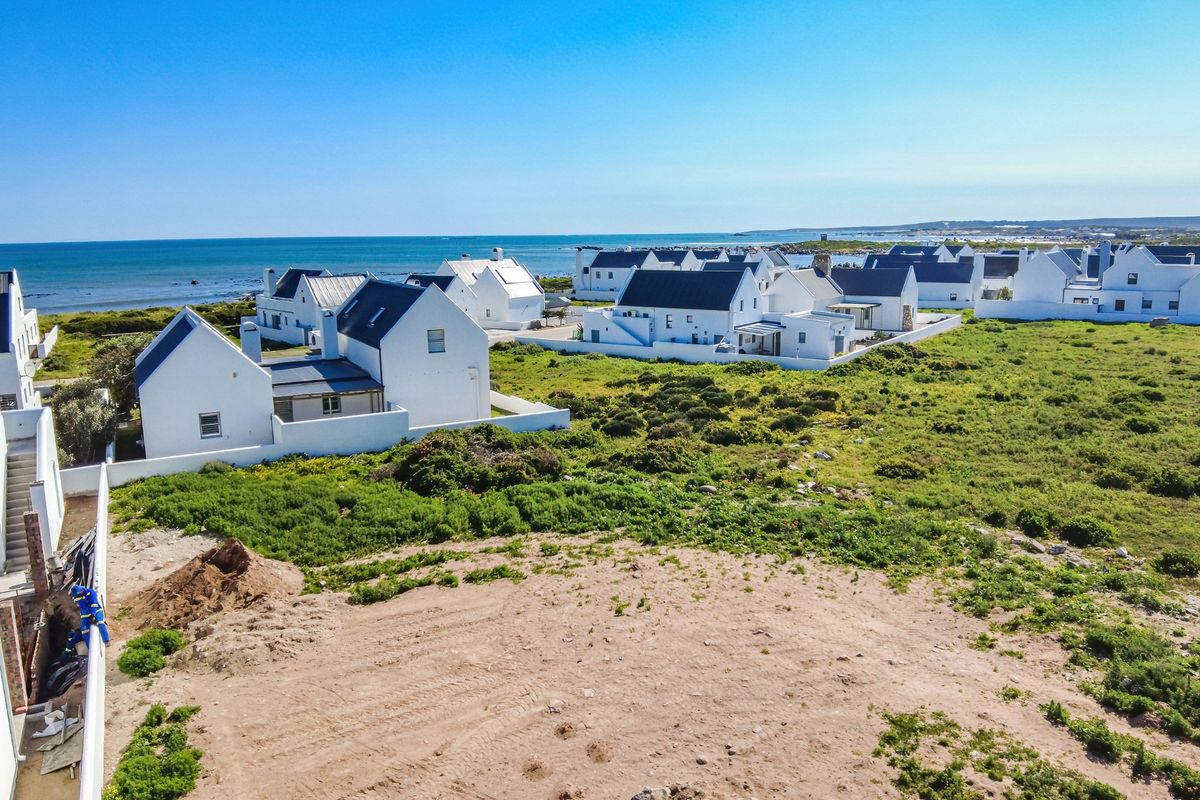 Aerial view of a coastal residential estate featuring white houses with dark roofs, situated near the ocean with surrounding natural vegetation.