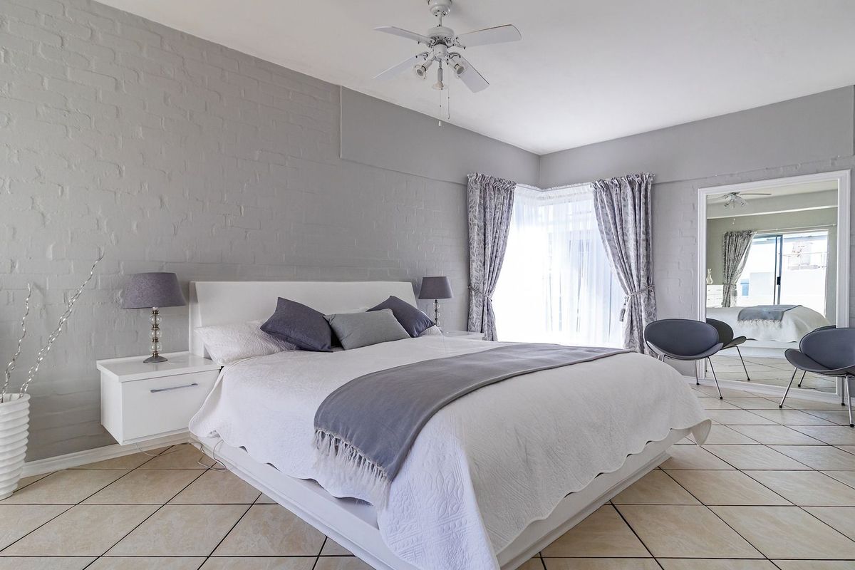 Spacious bedroom featuring neutral painted brick walls, tiled flooring, and a ceiling fan, offering a clean and well-maintained living space.