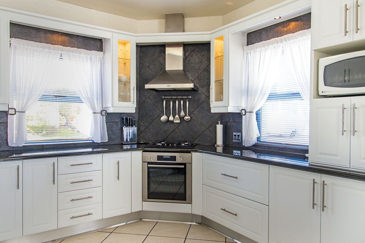 A well-maintained kitchen featuring white cabinetry, granite countertops, a tiled backsplash, and integrated stainless steel appliances including an oven and extractor fan.