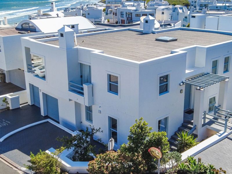 Aerial view of a modern coastal residence featuring a flat roof, integrated garage, and balcony, situated in a prime seaside estate.