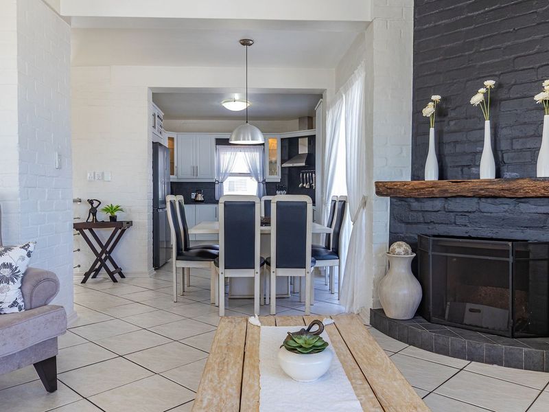 An open-plan living and dining area featuring a prominent black brick fireplace with a timber mantelpiece and tiled flooring throughout.