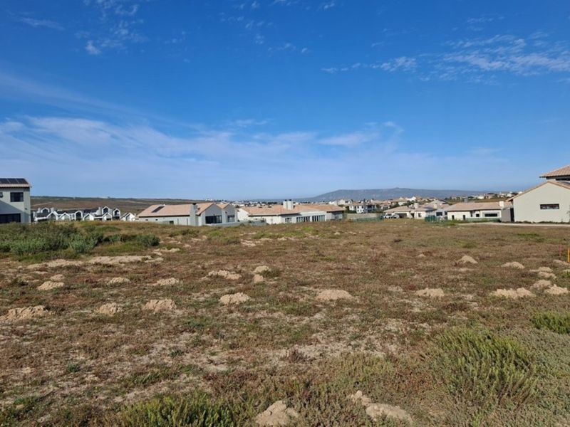 A view of a vacant residential plot with surrounding established housing in a coastal estate setting.
