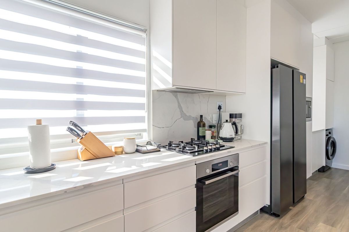 Modern kitchen featuring sleek handleless cabinetry, stone countertops, marble-look splashback, gas hob, and built-in oven, with integrated laundry space.