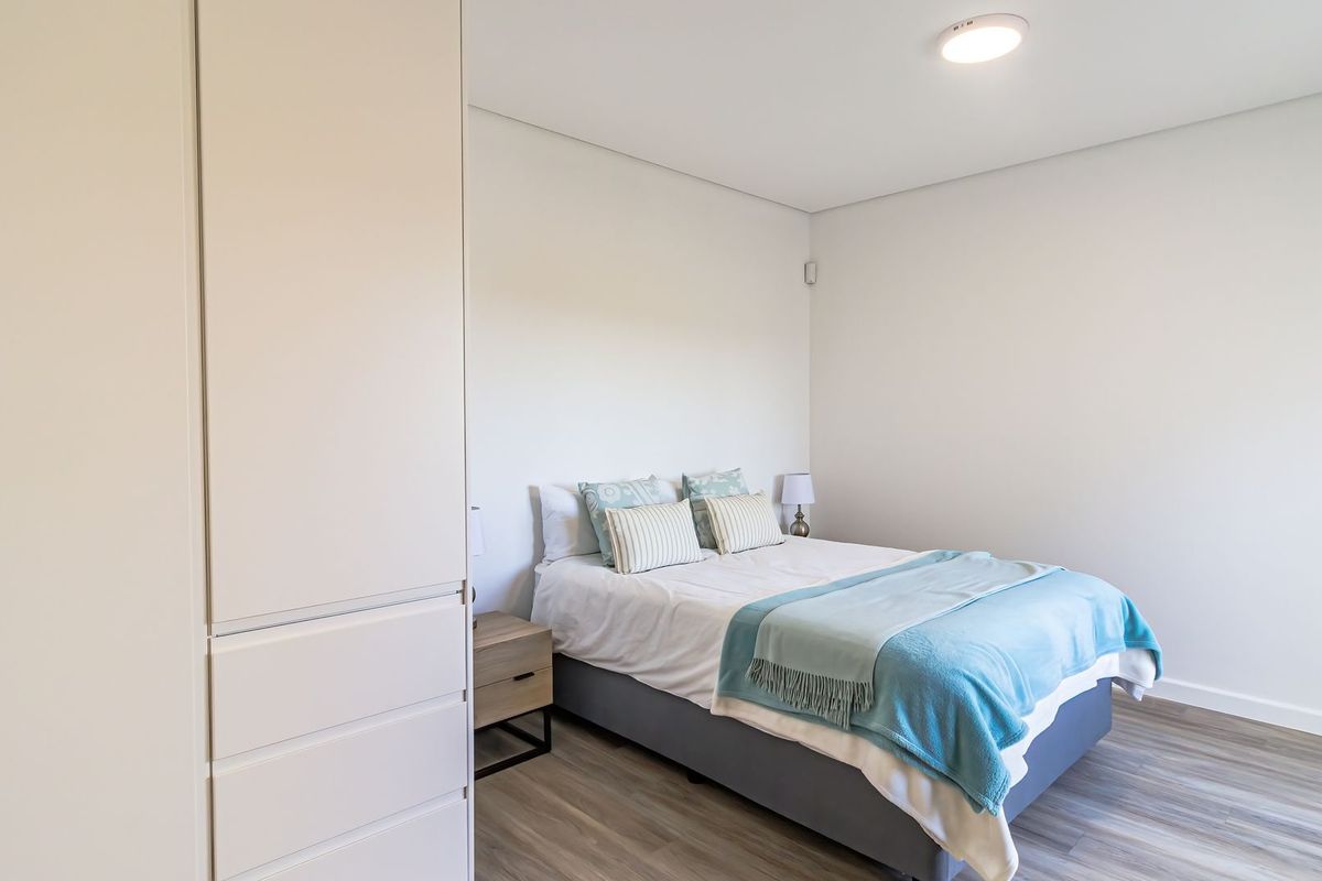A clean and well-maintained bedroom featuring neutral walls, modern laminate flooring, and a spacious built-in wardrobe.