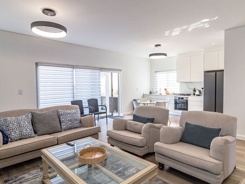 A bright, modern open-plan living and kitchen area featuring laminate flooring, contemporary pendant lighting, and seamless access to an outdoor patio.