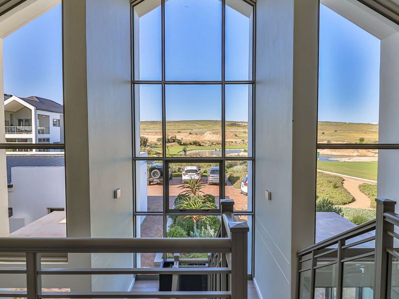 A bright, double-volume hallway featuring expansive floor-to-ceiling windows that provide natural light and scenic views of the surrounding estate.