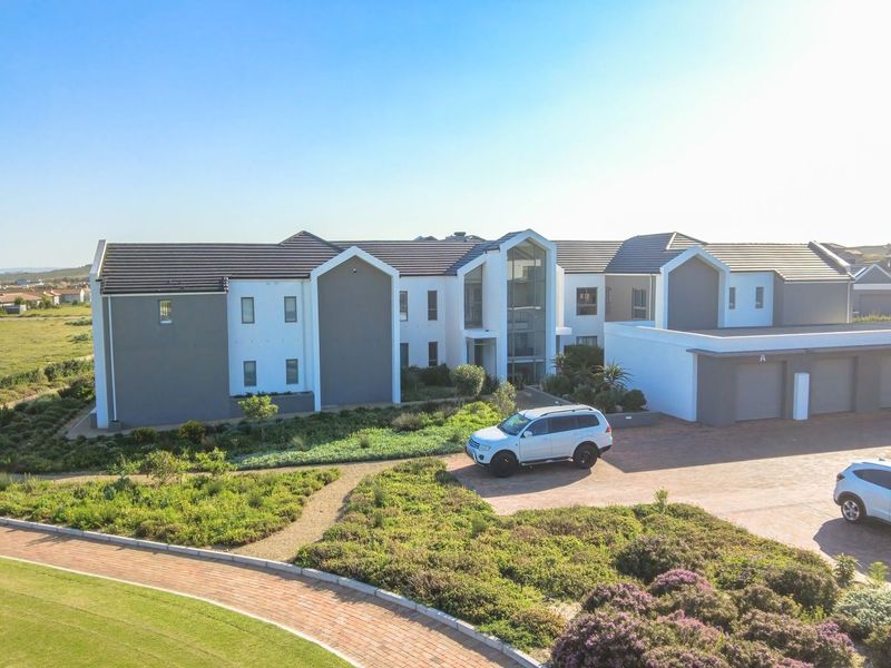 Aerial view of a modern apartment complex featuring a paved driveway, multiple garage units, and well-maintained landscaped garden areas.