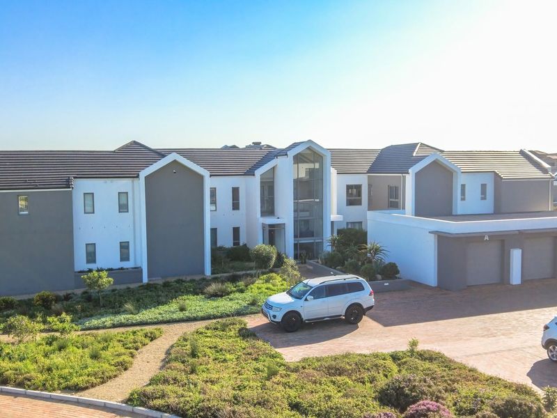 Aerial view of a modern apartment complex featuring a paved driveway, integrated garage units, and well-maintained landscaped garden areas.