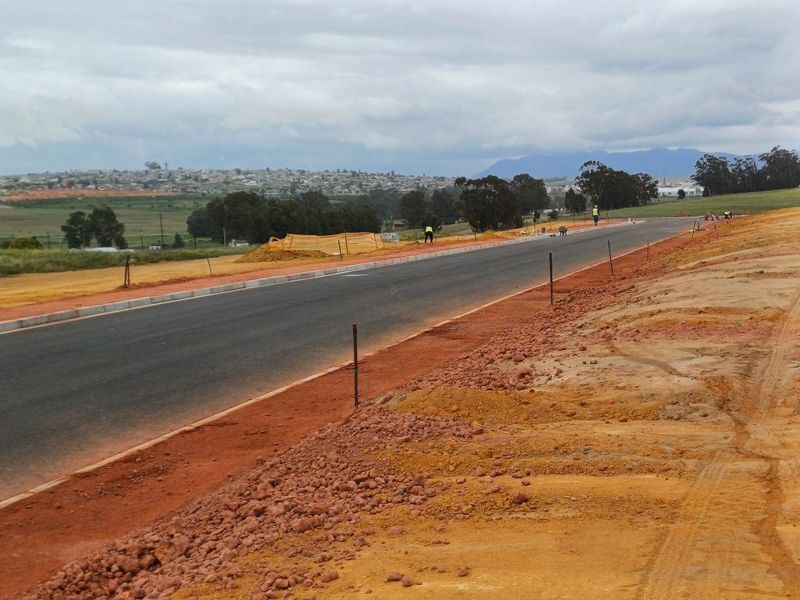 A view of an industrial access road under construction, featuring asphalt paving, concrete curbing, and surrounding undeveloped land.