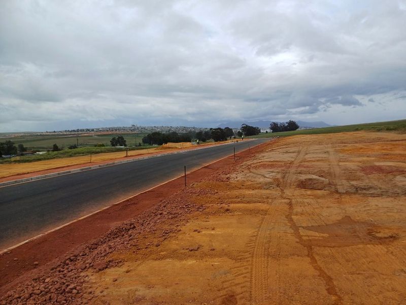 A view of a newly constructed asphalt road with concrete curbing, set within an undeveloped industrial or commercial land parcel.