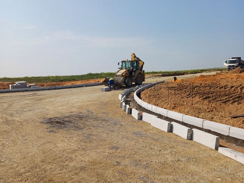 An industrial development site showing ongoing road construction with concrete kerbing installation and heavy machinery in operation.