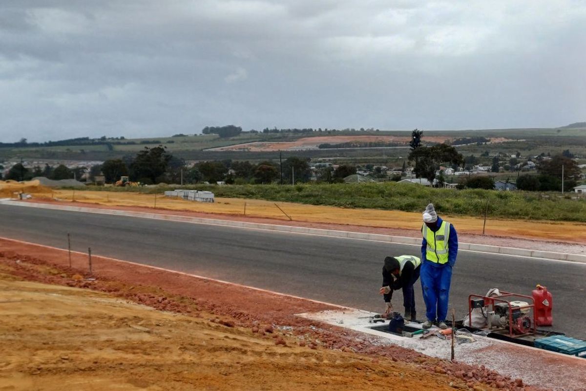 An industrial development site showing a newly paved asphalt road with concrete curbing and ongoing utility infrastructure installation.