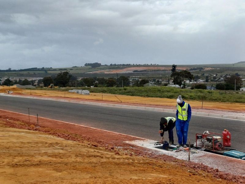 An industrial development site showing a newly paved asphalt road with concrete curbing and ongoing utility infrastructure installation.