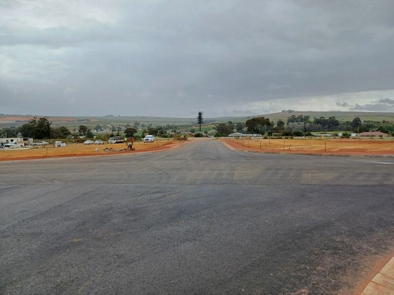 A view of a newly paved asphalt road within an industrial development site, featuring cleared land and surrounding landscape.