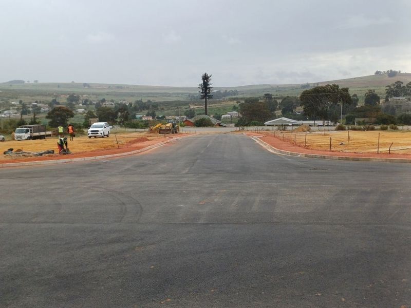 A view of a newly paved asphalt road with concrete curbing in an industrial development area under construction.