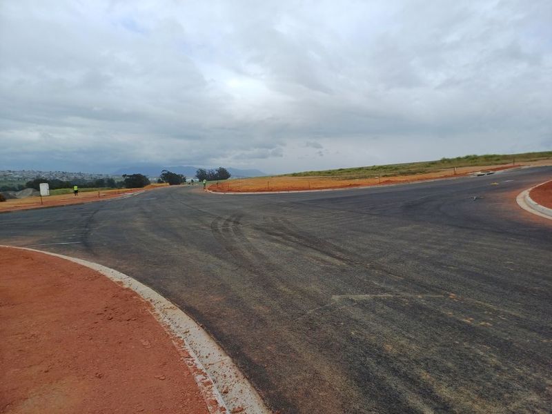 A view of a newly constructed asphalt road intersection with concrete curbing in an industrial development area.