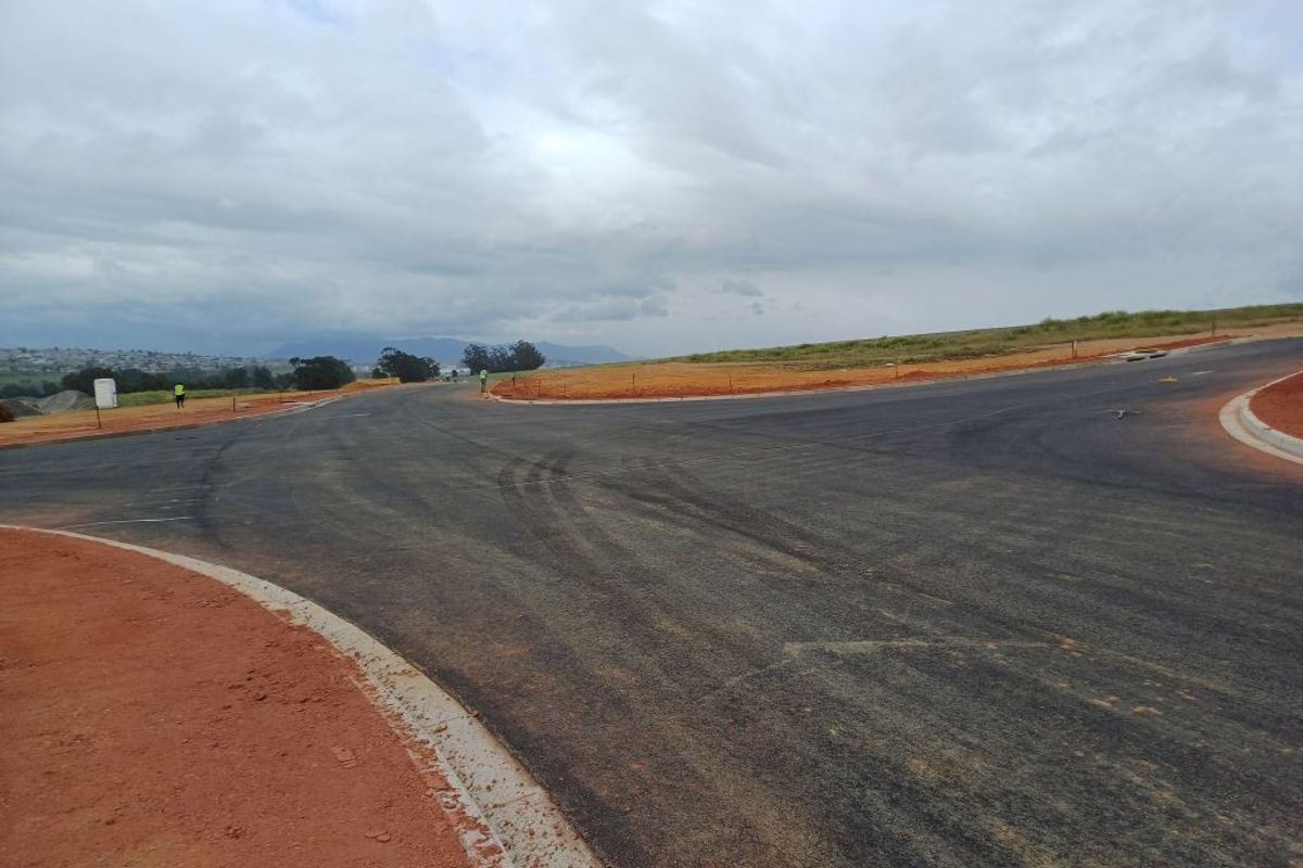 A view of a newly constructed asphalt road intersection with concrete curbing in an industrial development area.