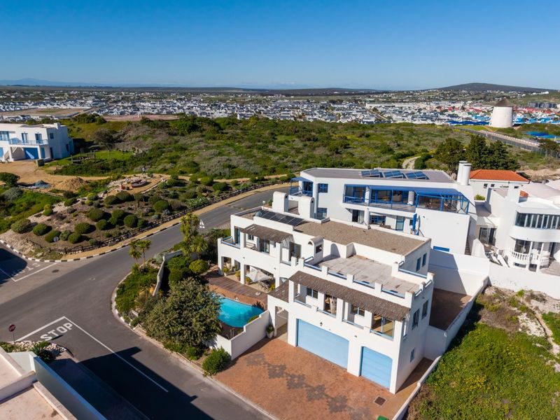 Aerial view of a multi-level residential property featuring a swimming pool, solar panels, and a double garage in a coastal setting.