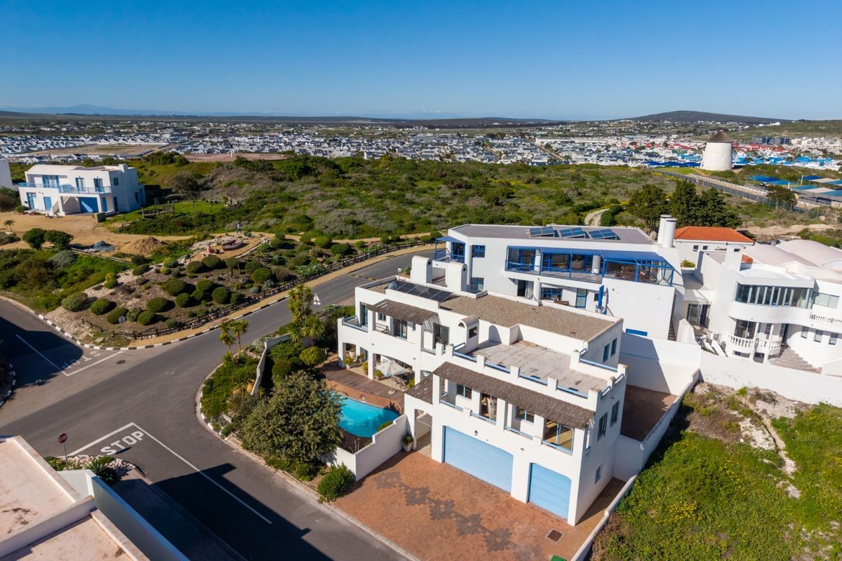 Aerial view of a multi-level residential property featuring a swimming pool, solar panels, and a double garage in a coastal setting.