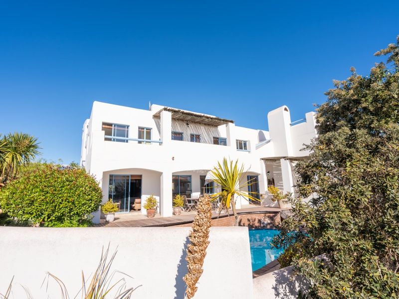 Rear elevation of a white multi-story house featuring a swimming pool, wooden decking, and a covered balcony area.