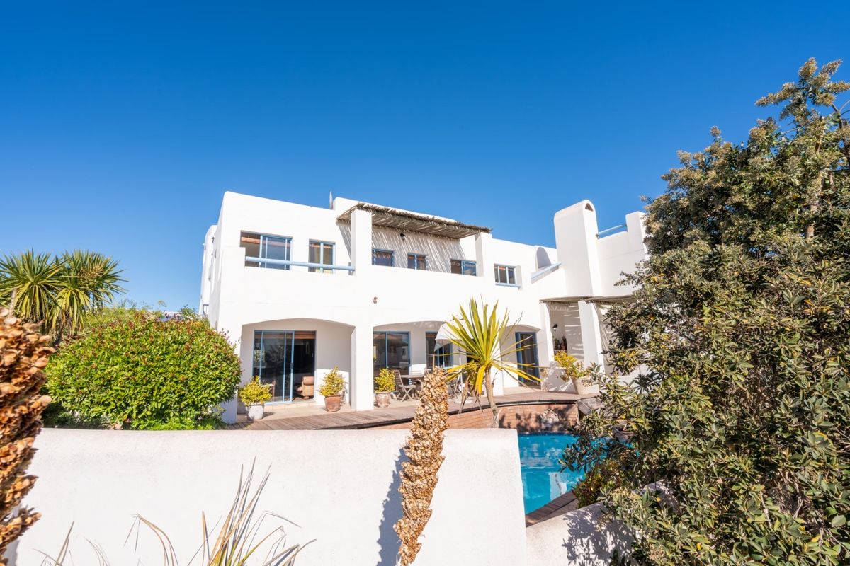Rear elevation of a white multi-story house featuring a swimming pool, wooden decking, and a covered balcony area.