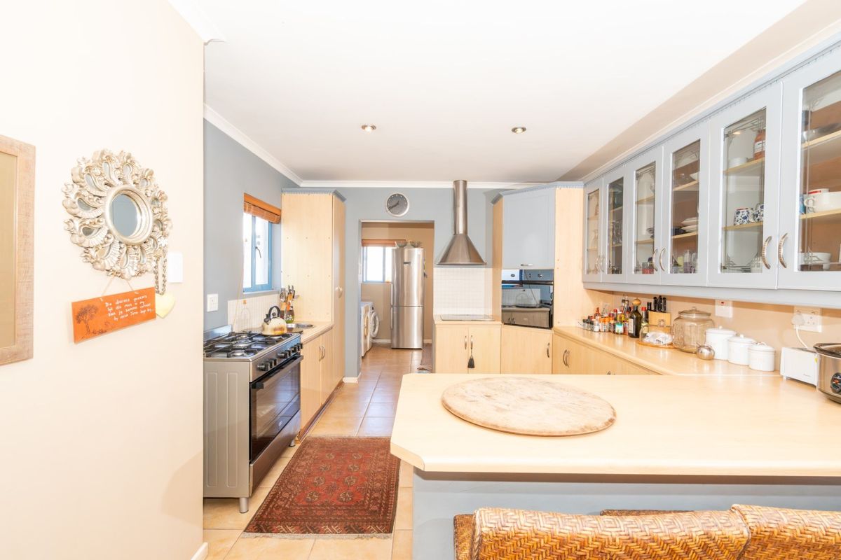 A functional kitchen featuring light wood cabinetry, glass-fronted display cupboards, gas stove with extractor, and tiled flooring, with an adjacent scullery area.