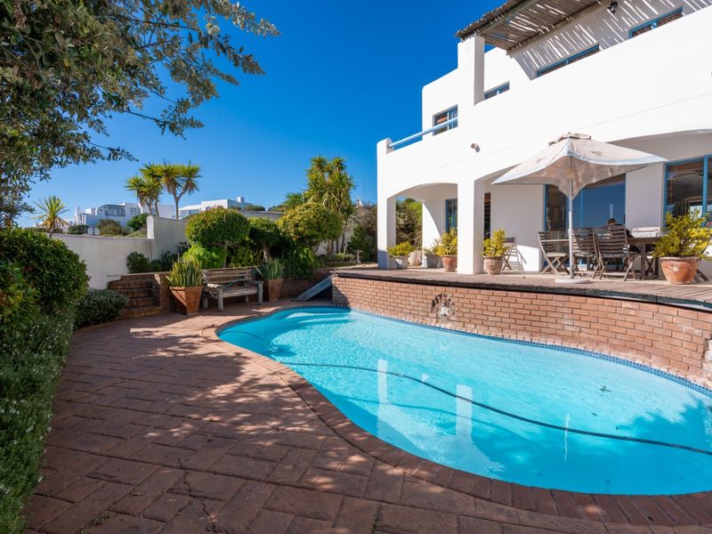 Outdoor pool area featuring a swimming pool with brick coping, adjacent timber decking, and a covered patio area attached to the main residence.