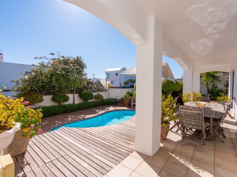 A covered patio area featuring tiled flooring and timber decking, overlooking a private swimming pool and landscaped garden.