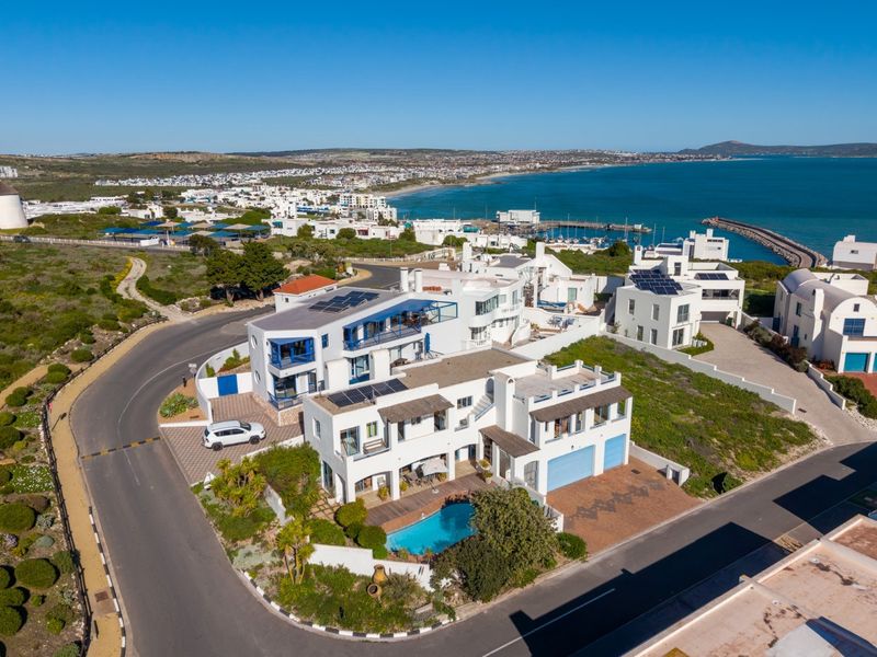 Aerial view of a coastal property featuring a swimming pool, solar panels, and multiple balconies, situated near the ocean and local harbour.