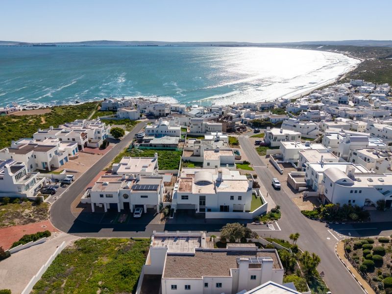An aerial view of a coastal residential estate featuring white houses, paved streets, and proximity to the ocean.