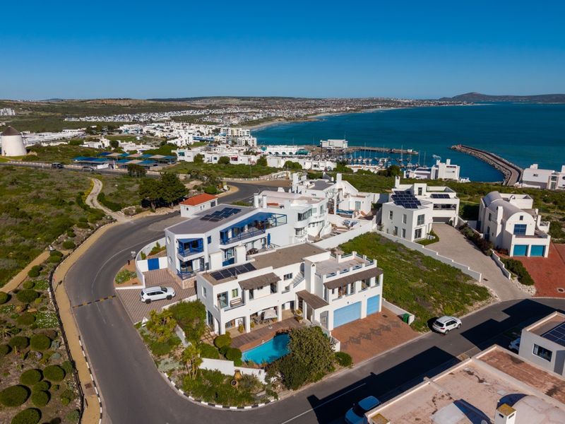 Aerial view of a coastal residential property featuring a swimming pool, solar panels, and proximity to the harbor and coastline.