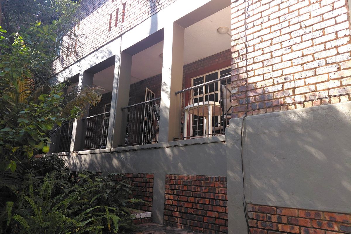 Rear view of the apartment building featuring an exposed brick facade, a covered patio area with metal railings, and direct access via sliding glass doors.