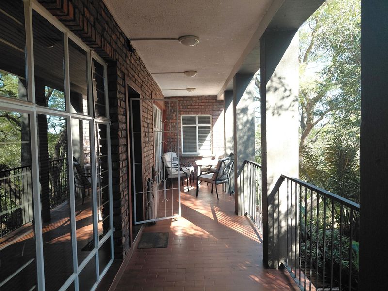 A covered balcony featuring exposed brick walls, tiled flooring, and a metal balustrade, offering a sheltered outdoor space with natural light.