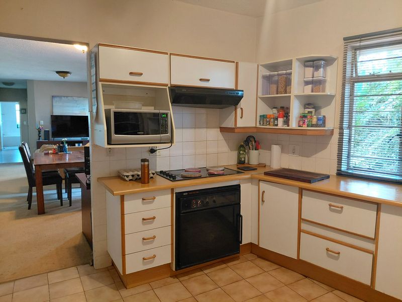 A functional kitchen featuring built-in cabinetry, an electric hob, an oven, and tiled splashbacks, with an open-plan layout connecting to the dining area.