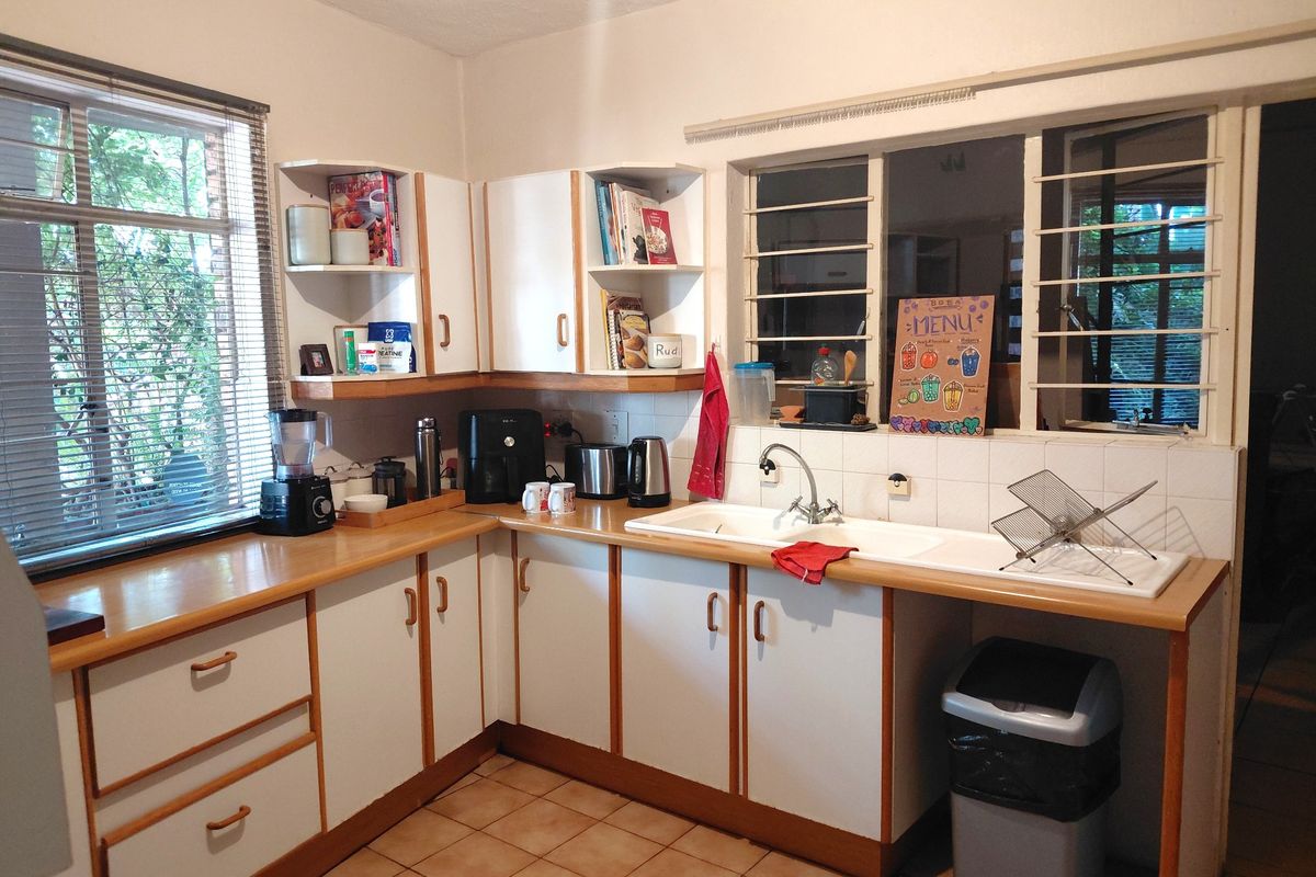 A functional kitchen featuring laminate countertops, a double basin sink, tiled flooring, and ample built-in cabinetry with security bars on the windows.