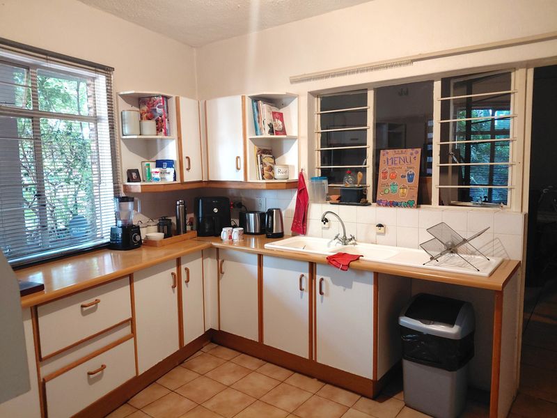 A functional kitchen featuring laminate countertops, a double basin sink, tiled flooring, and ample built-in cabinetry with security bars on the windows.