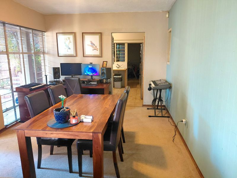 Dining room area featuring carpeted flooring and large windows with venetian blinds, providing a functional space with access to the adjacent room.