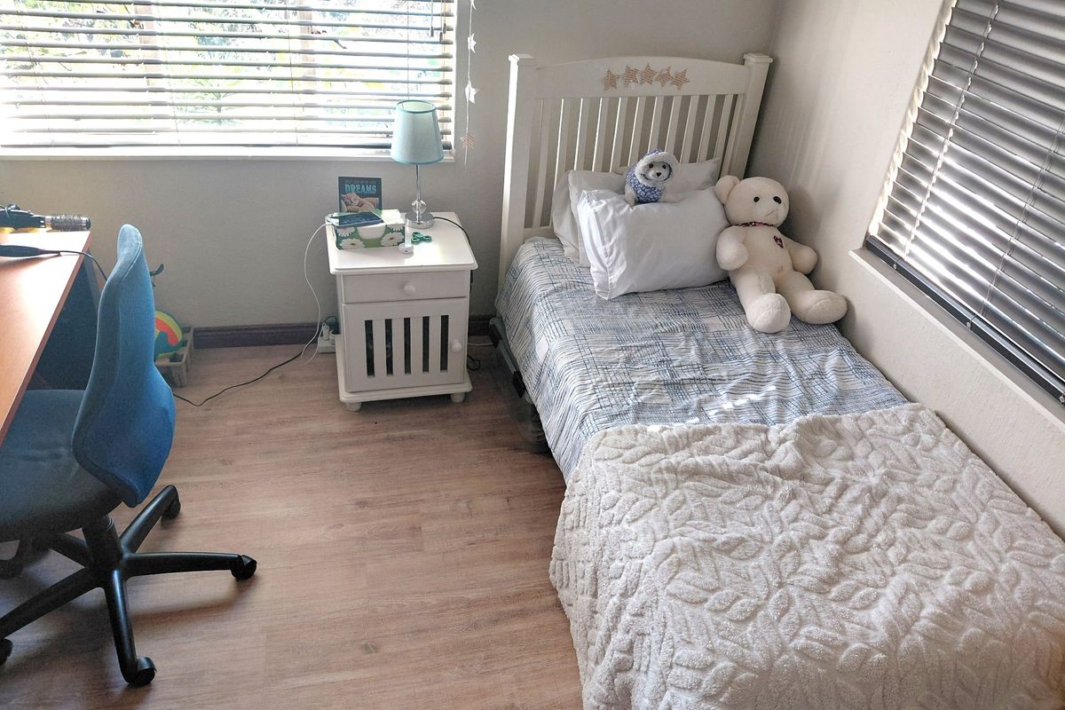 A well-lit bedroom featuring light-toned laminate flooring and dual windows with fitted venetian blinds.