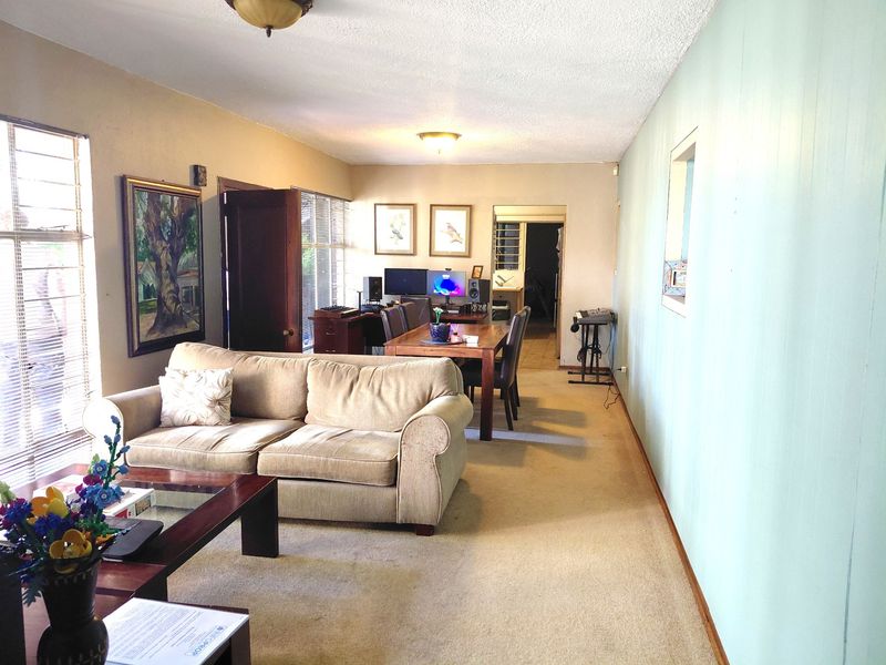 An open-plan living and dining area featuring carpeted flooring, window blinds, and neutral wall tones, offering a functional layout for daily living.