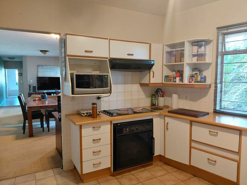 A functional kitchen featuring white cabinetry with wood trim, laminate countertops, built-in oven, electric hob, and tiled backsplash, with an open view to the living area.