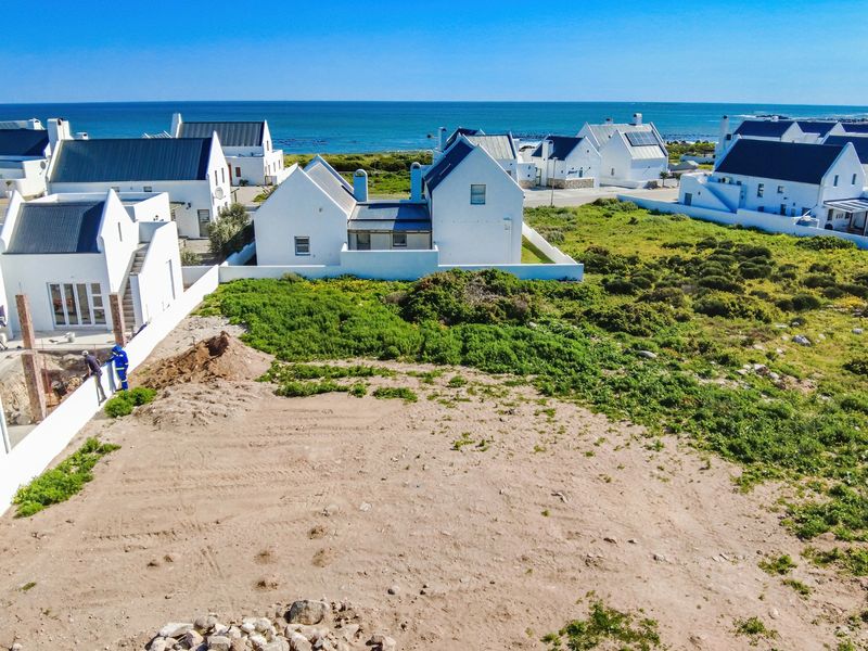 Aerial view of a vacant residential plot situated in a coastal estate, featuring surrounding white-walled homes and proximity to the ocean.