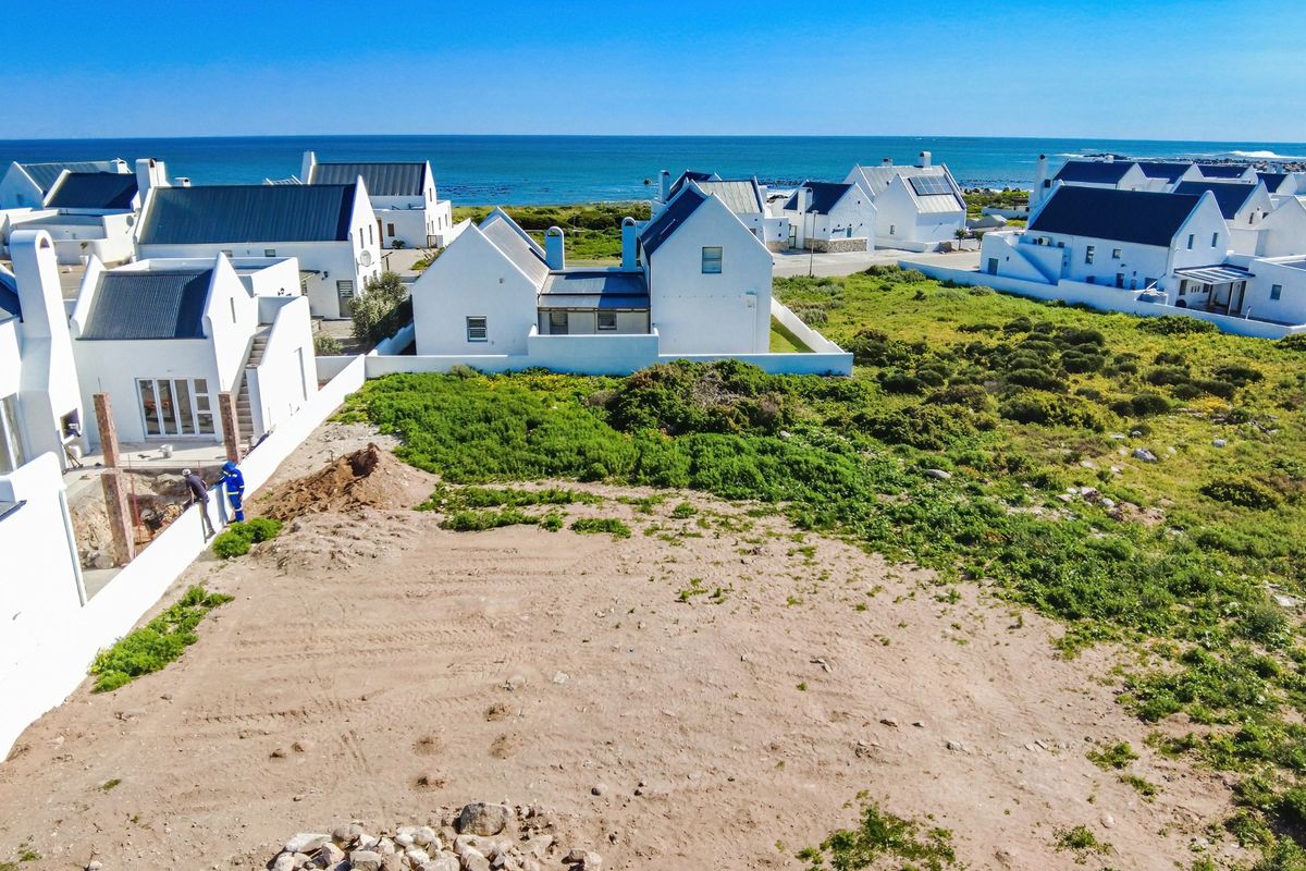 Aerial view of a vacant residential plot situated in a coastal estate, featuring surrounding white-walled homes and proximity to the ocean.