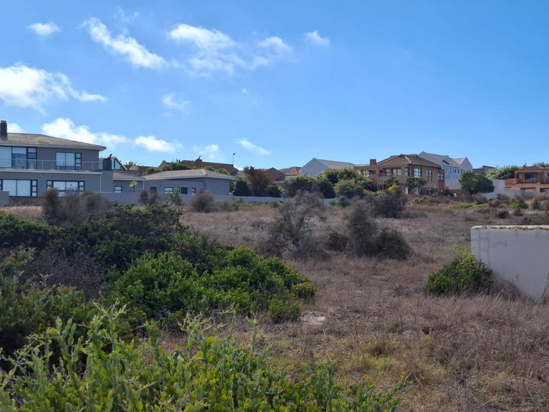 A view of a vacant residential plot featuring natural vegetation and surrounding established residential properties.