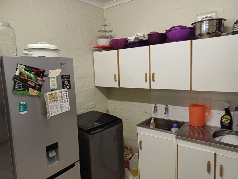 Functional laundry area featuring built-in cabinetry, a stainless steel sink, and tiled splashback, providing practical utility space.