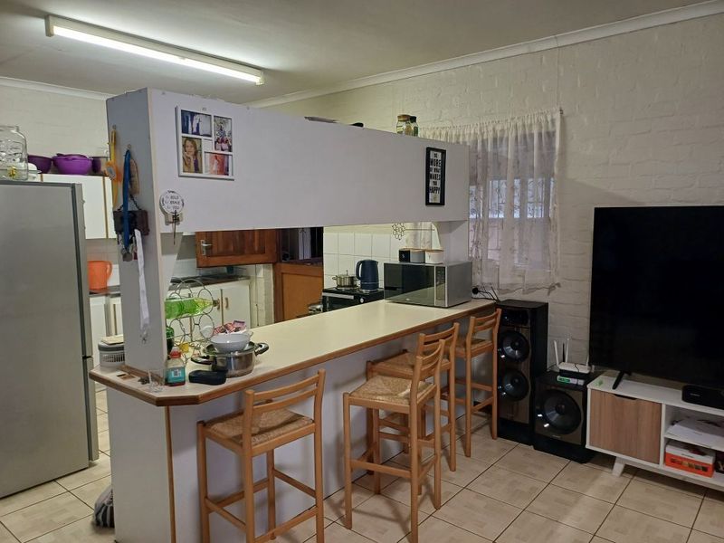 Open plan kitchen and living area featuring a breakfast bar, tiled flooring, and painted brick walls, offering a functional layout for daily living.