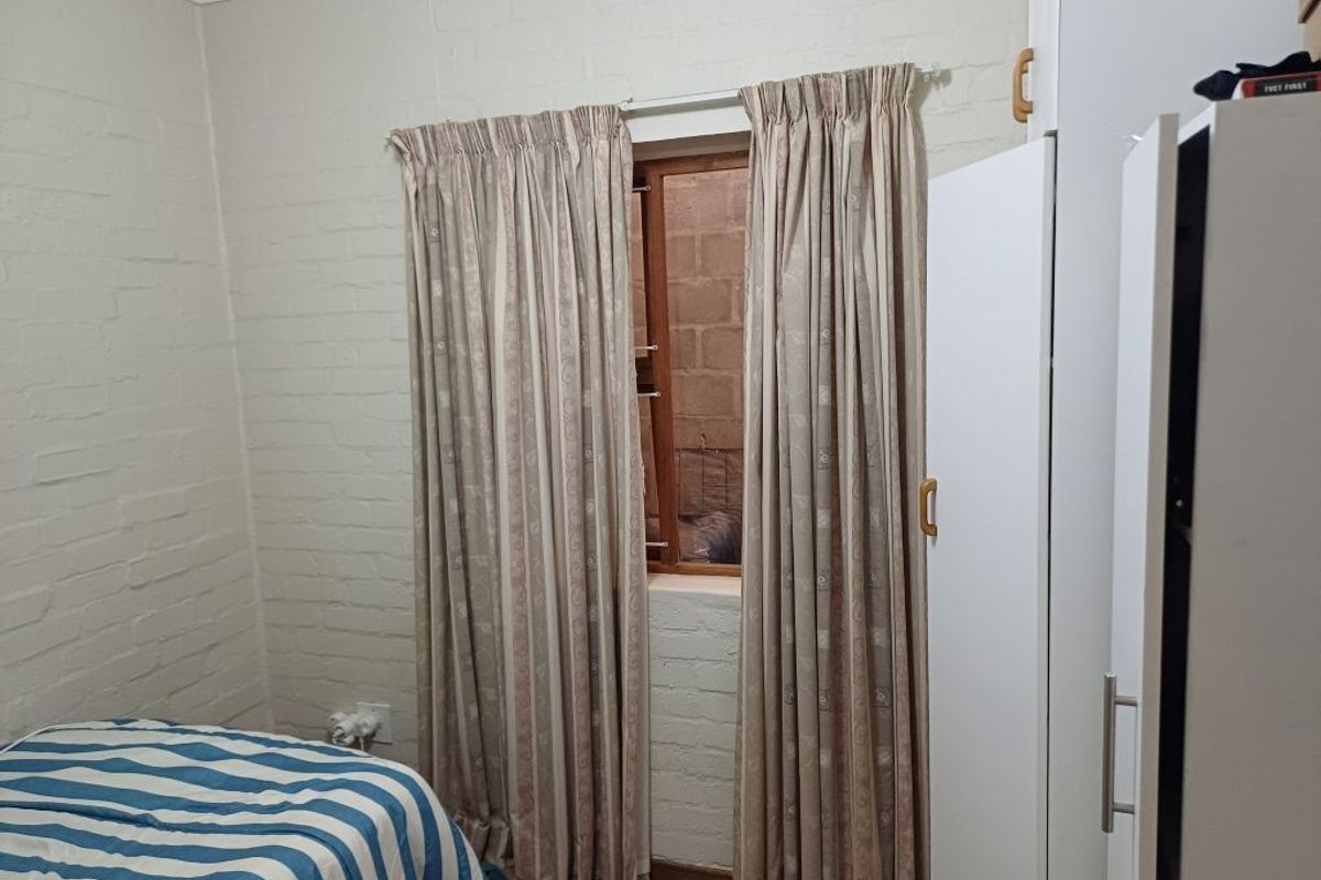 A bedroom featuring painted brick walls, a timber-framed window, and built-in wardrobe storage.