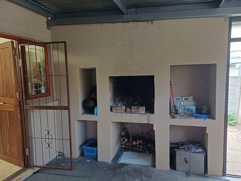 Covered patio area featuring a built-in brick braai with integrated storage niches and direct access to the garden.