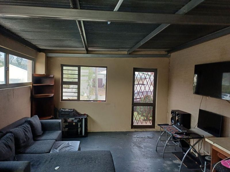 A living area featuring exposed steel beams, corrugated metal ceiling, painted brick walls, and aluminium window frames with a security gate.